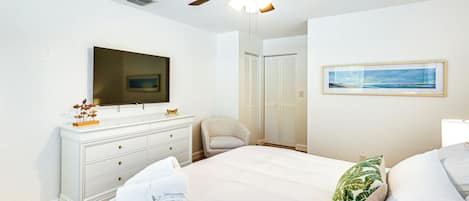 A bedroom with a bed, a dresser, a television, a ceiling fan, a chair, a closet, and a framed picture on the wall.