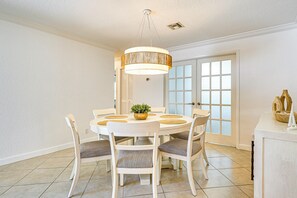 Un área de comedor con una mesa redonda, sillas blancas, una lámpara colgante y vistas a través de una puerta de vidrio.