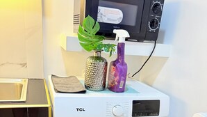 Eine Waschmaschine mit Frontöffnung, ein Bedienfeld, eine Mikrowelle darüber und eine Pflanze obenauf.