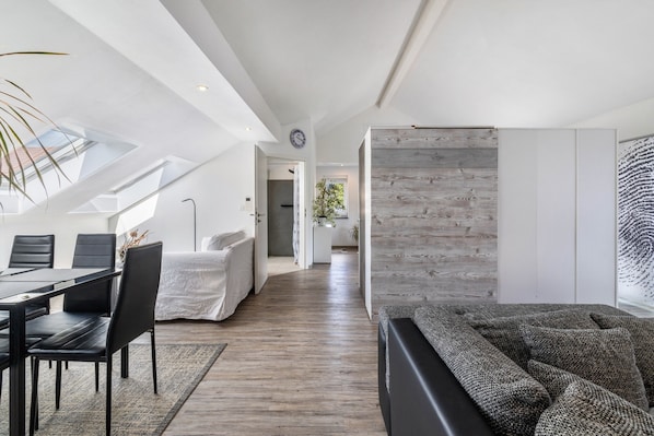 A modern interior with a dining area, a sofa, a wooden accent wall, and a skylight.
