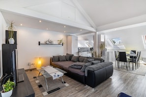 A modern living room with a sofa, a dining area, a TV, and a staircase leading to an upper level. - Holiday Apartment with Terrace, Garden & BBQ – Pets Welcome (Balingen)