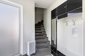 A hallway with a white door, a staircase with grey carpeted steps, a white radiator, and a black cabinet with hooks.
