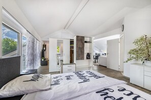 A modern bedroom with a large bed, a walk-in closet, and a view of the outdoors.