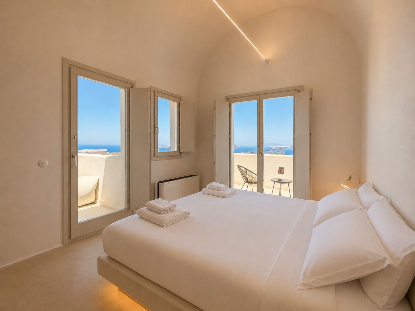 A bedroom with a bed, two windows, and a view of the sea.