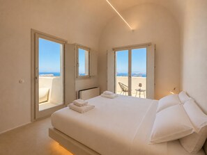 A bedroom with a bed, two windows, and a view of the sea. - Vespera Private Luxury Suites (Santorini)