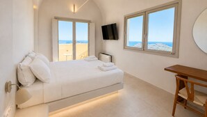 A modern bedroom with a bed, a TV, a desk, and a view of the sea. - Vespera Private Luxury Suites (Santorini)