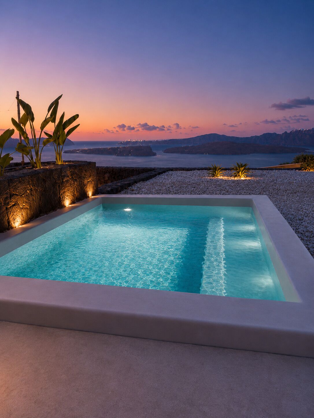 A rectangular pool with clear water, surrounded by a pebble beach and plants, with a sunset view in the background.