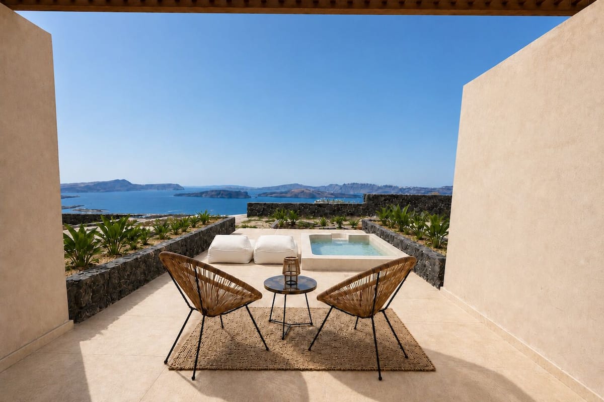 A terrace with a view of the sea, two wicker chairs, a small table, and a pool.