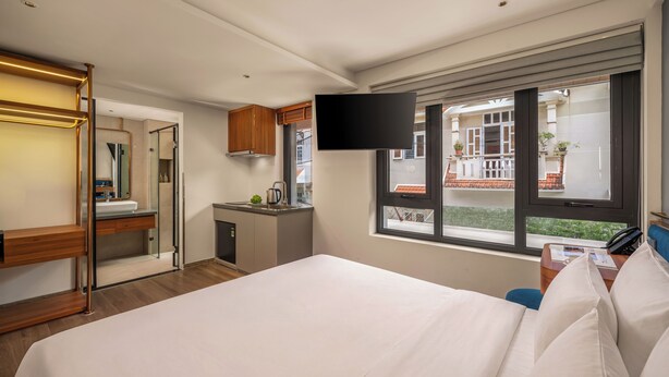 A hotel room with a bed, a TV mounted on the wall, a desk with a phone, and a window with a view of the outside. - Xhome Da Nang Hotel and Suite  (Da Nang)