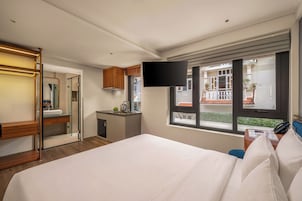 Quarto de hotel com uma cama, televisão fixada na parede, escrivaninha com telefone e janela com vista para o exterior.
