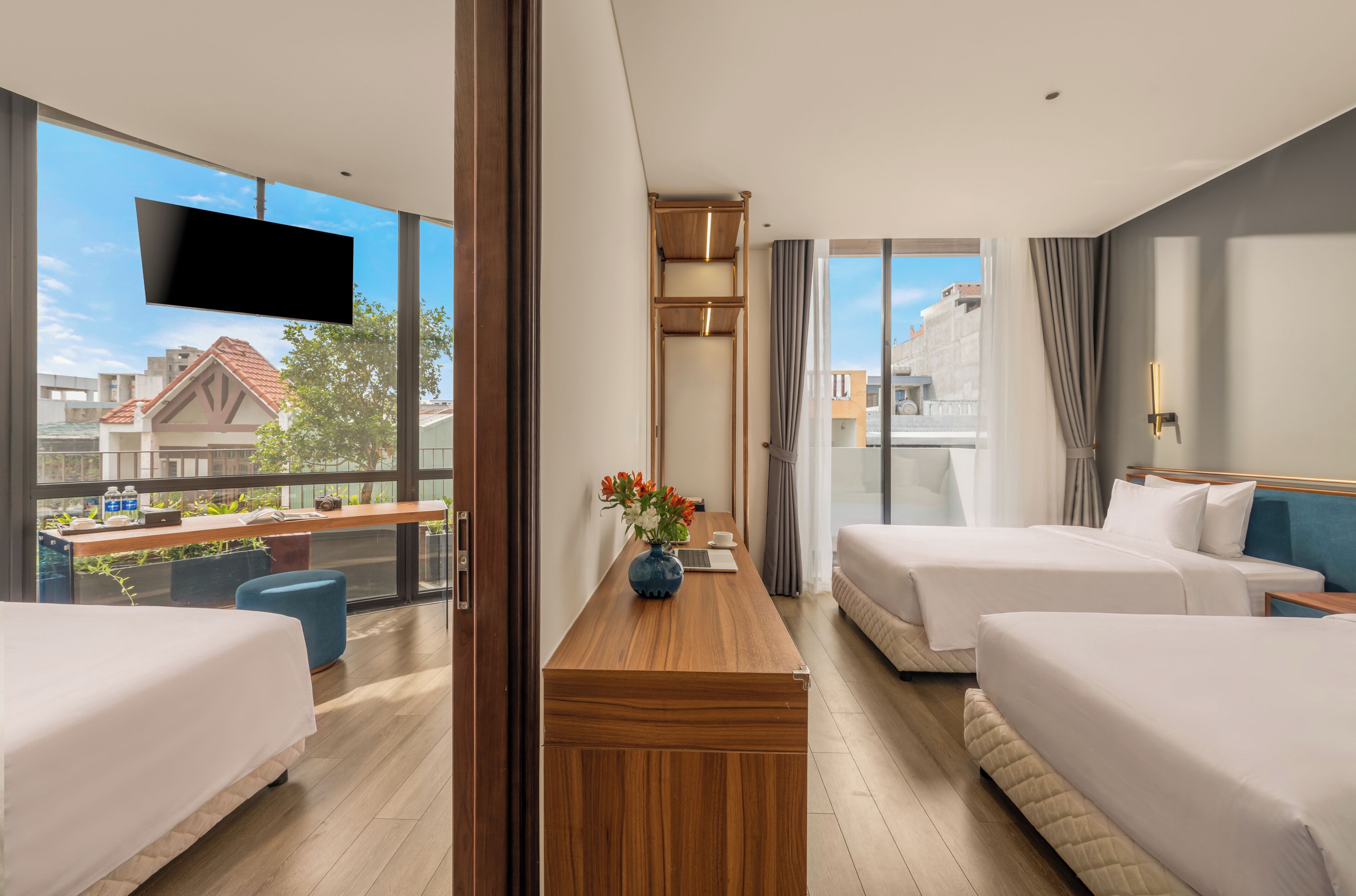 A hotel room with two beds, a wooden desk, a TV, and a view of buildings.
