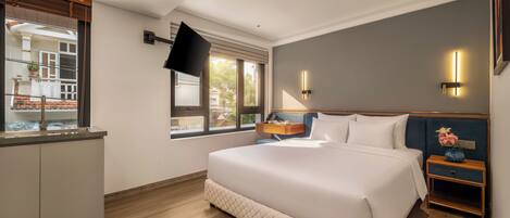 Habitación de hotel con cama, mesita de noche, televisor montado en la pared y ventana con vista a edificios.