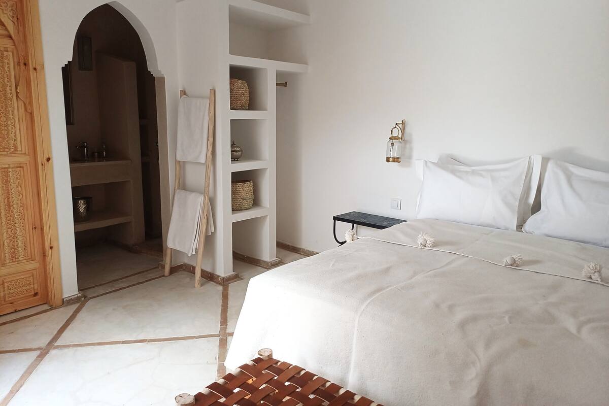A bedroom with a bed, a wardrobe, shelves, a nightstand, and a lamp.