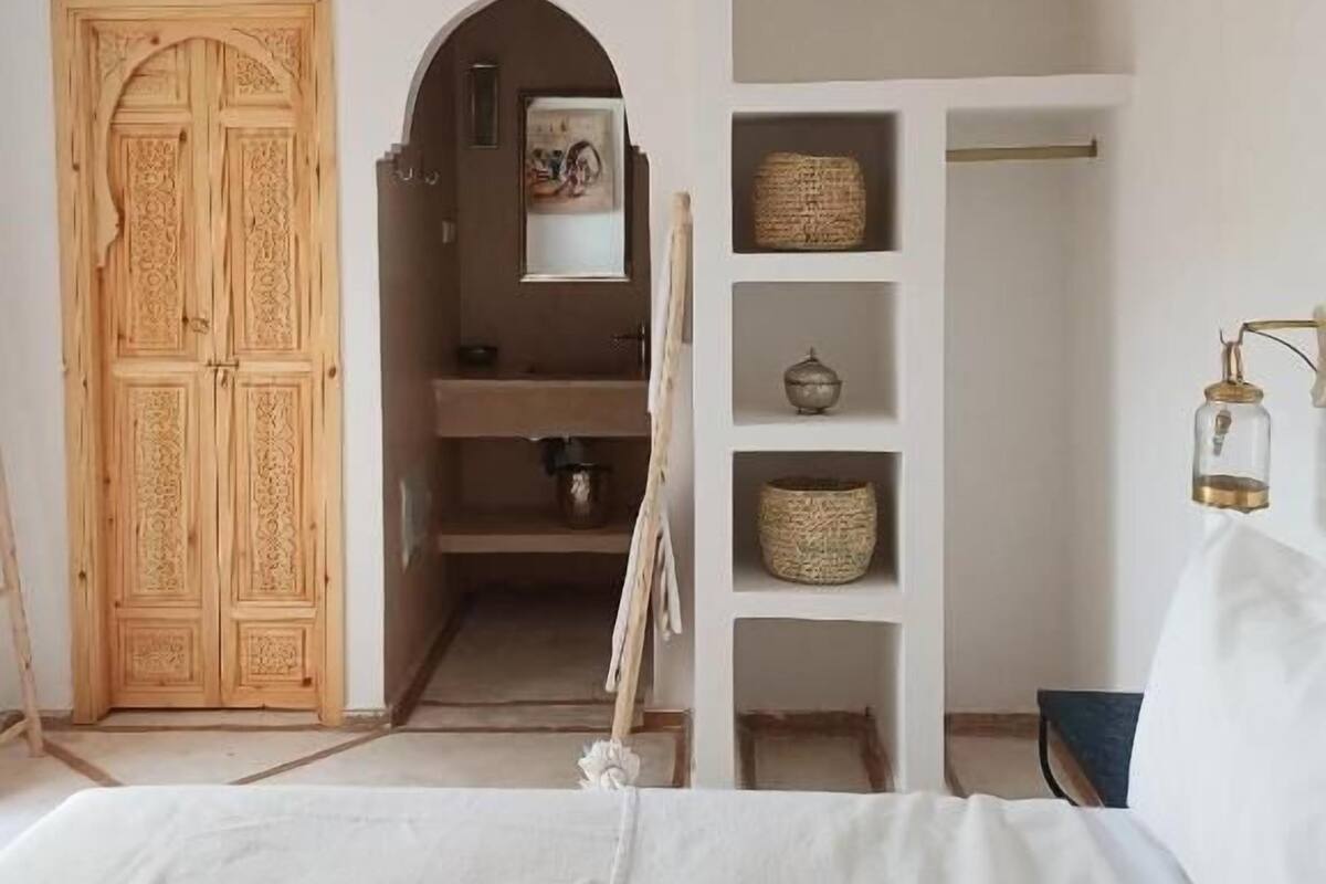 A bedroom with a bed, a wardrobe, a mirror, and a shelf with baskets.