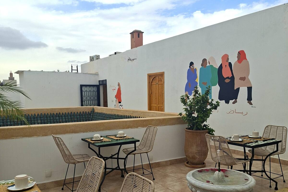 An outdoor patio with wicker chairs, a table set for dining, a decorative fountain, and a mural on the wall.