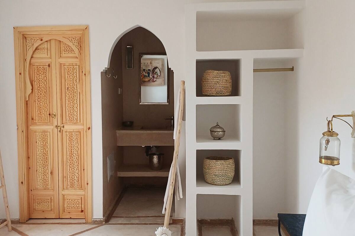 A bedroom with a bed, a wardrobe, a shelf with baskets, and a hanging lamp.
