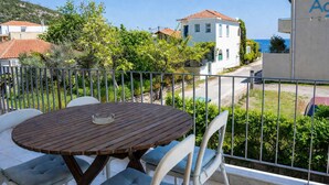 A balcony with a wooden table and chairs, overlooking a coastal area with houses and greenery.