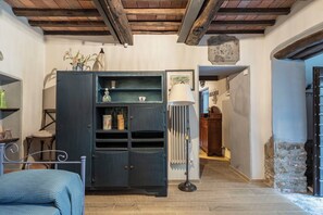 Una stanza con un letto, un armadio scuro con scaffali, una lampada da terra e un muro in pietra.