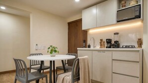 A compact kitchen with a white countertop, a microwave, a coffee maker, and a blender. There is a round table with four chairs and a potted plant. - Passiflora luxury suite (Cali)
