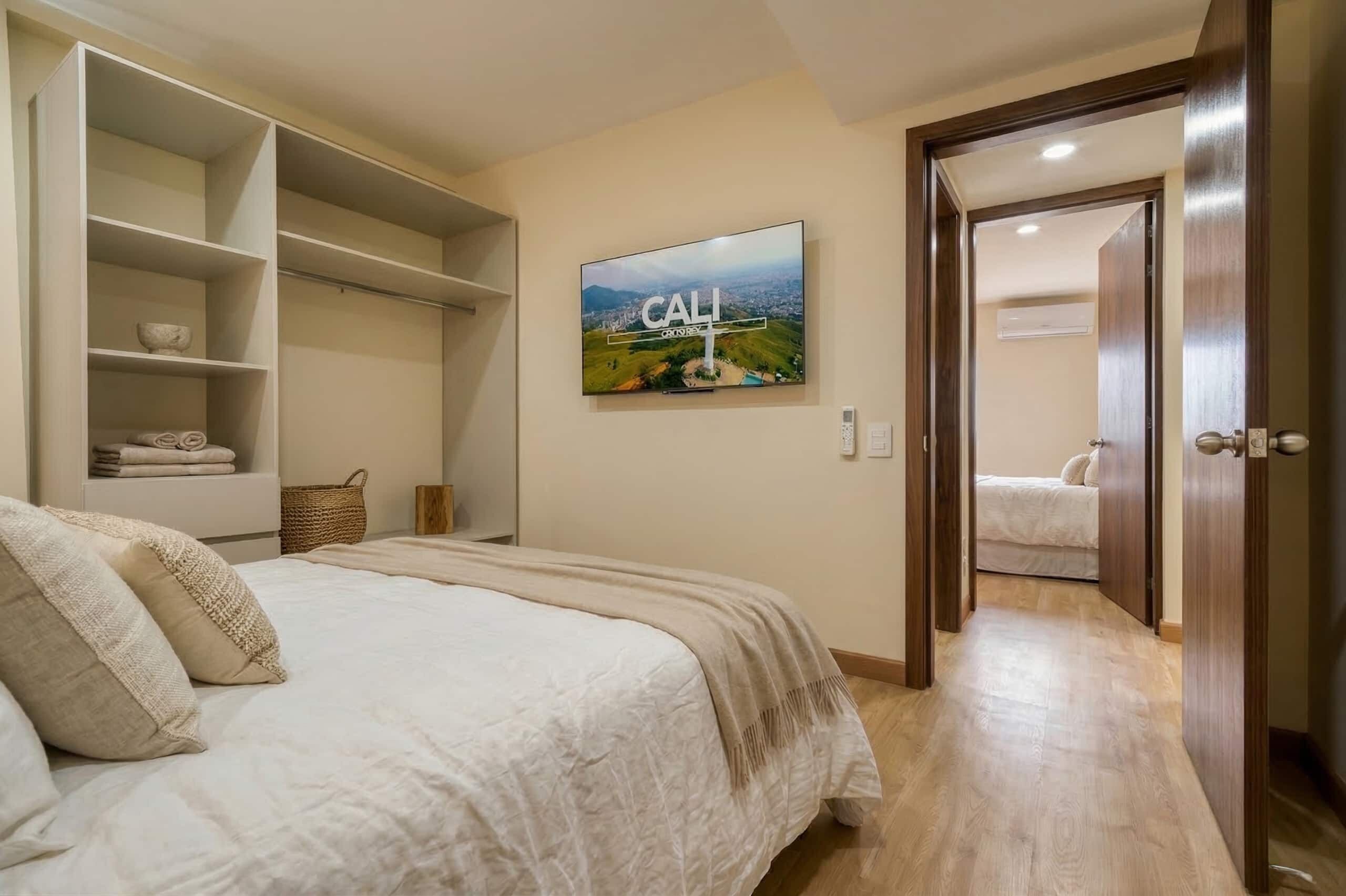 A bedroom with a bed, a wardrobe, a television, and a door leading to another room.