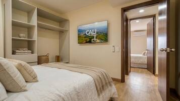 A bedroom with a bed, a wardrobe, a television, and a door leading to another room.