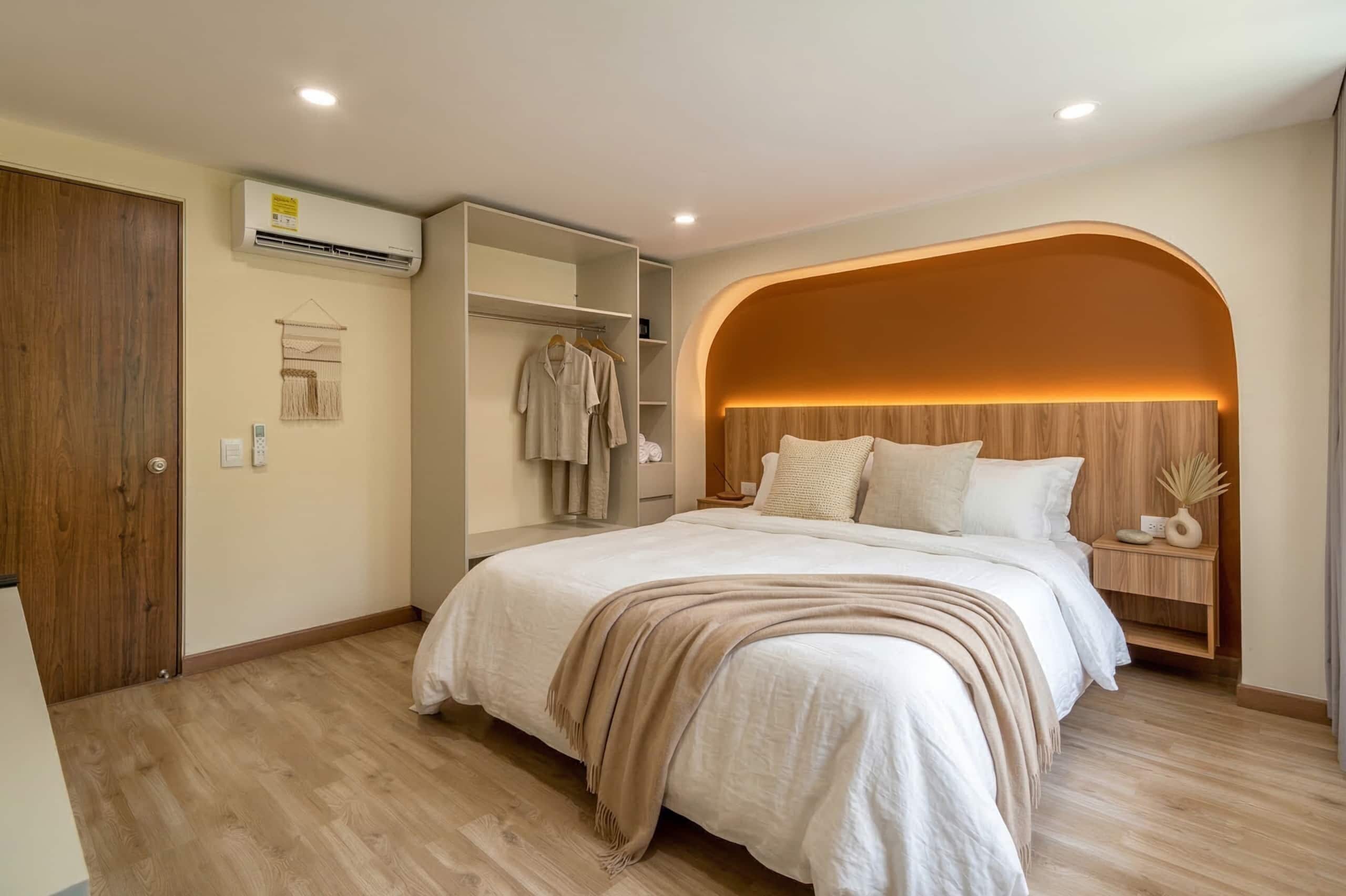 A bedroom with a bed, a wardrobe, a bedside table, and an arched wall design.