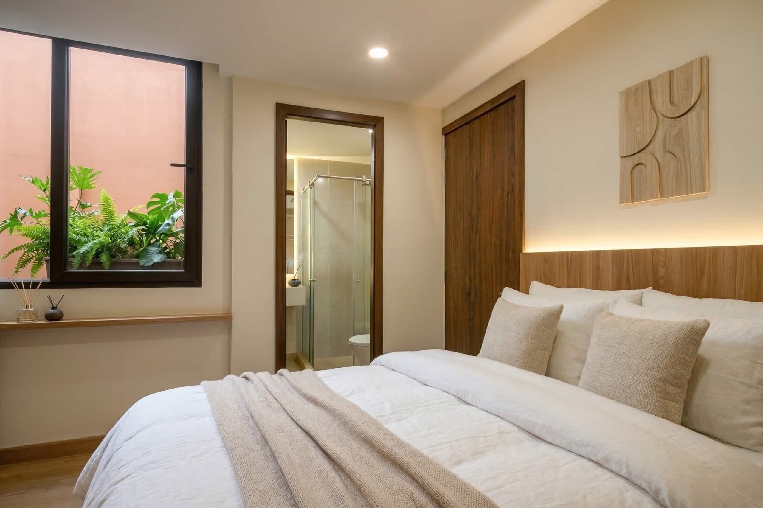 Un dormitorio con una cama grande, una ventana con plantas, un armario de madera y una zona de ducha.