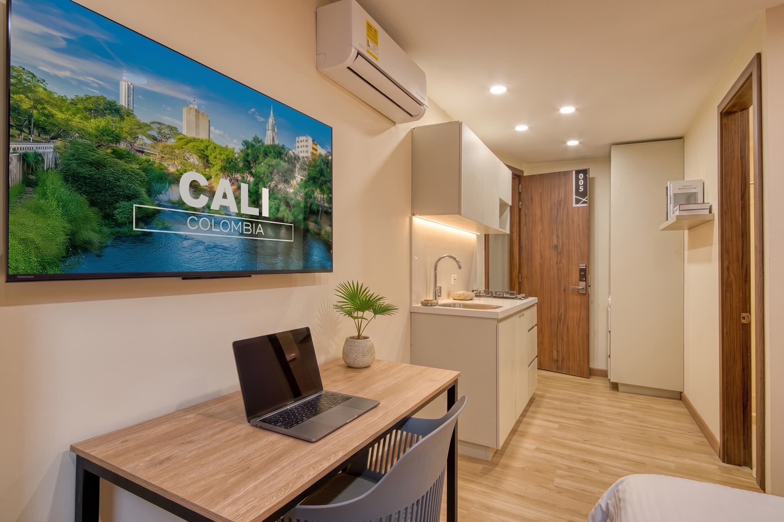 Quarto de hotel moderno com um laptop em uma escrivaninha, pia, espelho e uma porta com o símbolo de número.