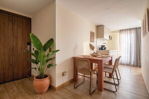 A dining area with a wooden table, wicker chairs, a potted plant, and a kitchen in the background. - Passiflora luxury suite (Cali)