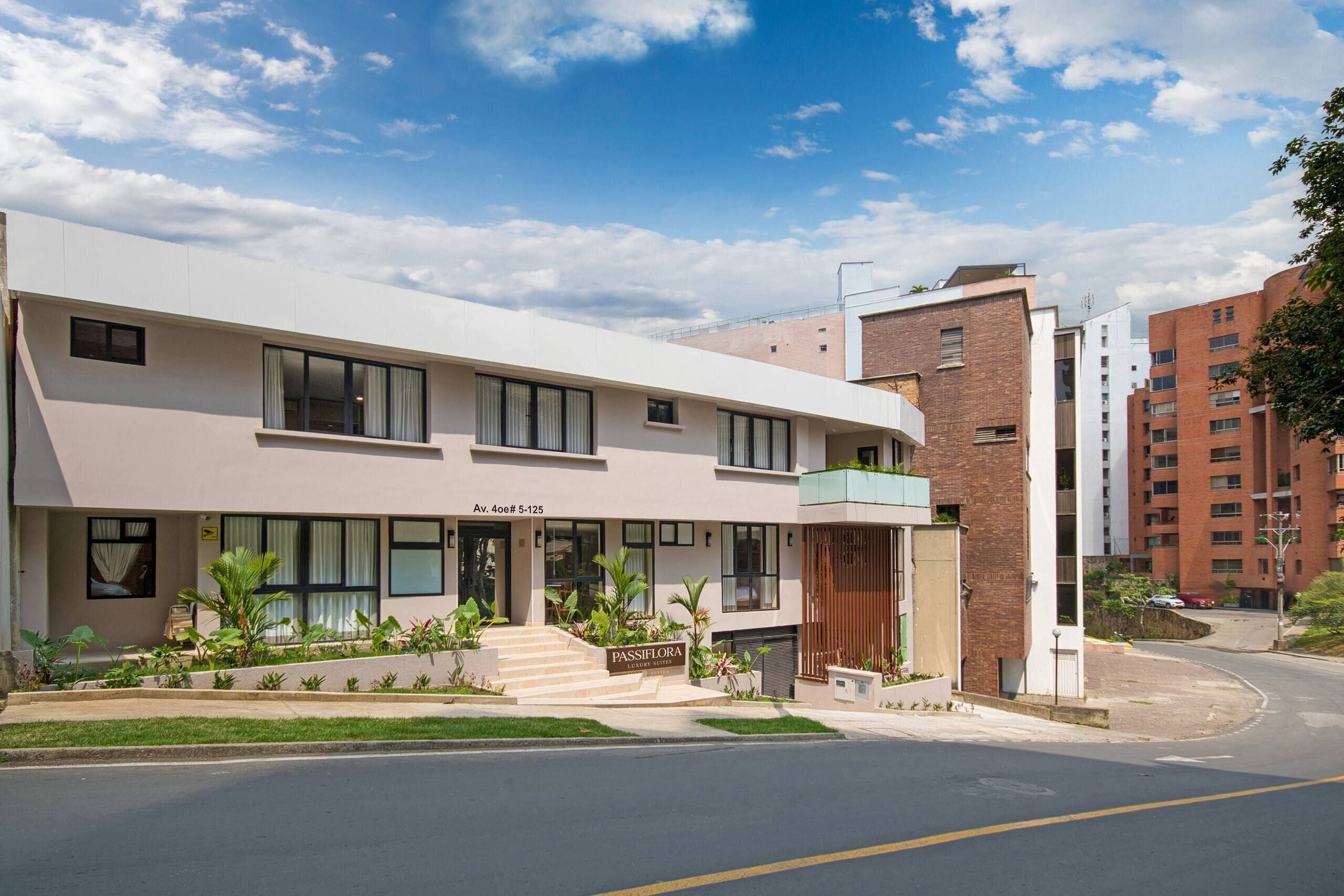 A modern building with a flat roof, large windows, and a sign indicating 'PASSIFLORA LUXURY SUITES.'