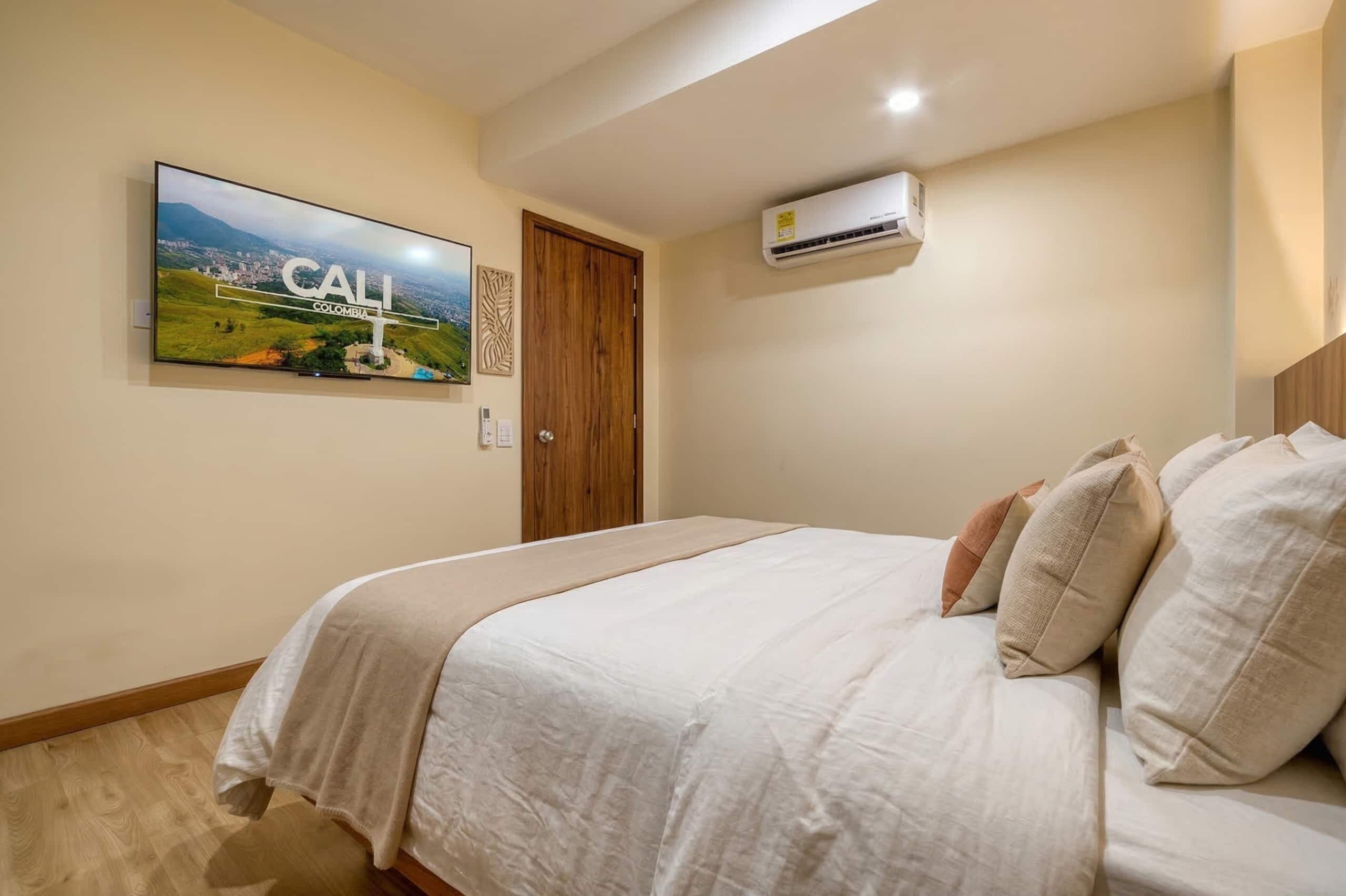 Een slaapkamer met een bed, een wandairconditioner, een deur en een aan de muur hangend landschapsbeeld.