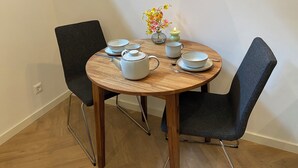 Una mesa de madera redonda con cuatro sillas, un florero con flores, una vela y un juego de té.