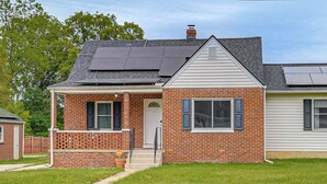 Una casa de dos pisos con fachada de ladrillo, un porche delantero y paneles solares en el techo.