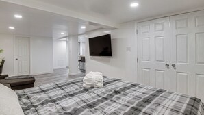 Un dormitorio con cama, televisor montado en la pared, armario y baño a la vista al fondo.