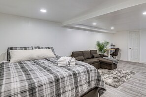 A bedroom with a bed, a sofa, a desk, and a plant.