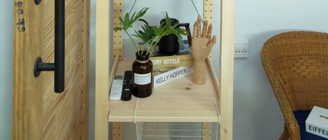 A wooden wardrobe with a hanging shelf, a small shelf with a plant and a hand-shaped object, and a chair with a box on it.
