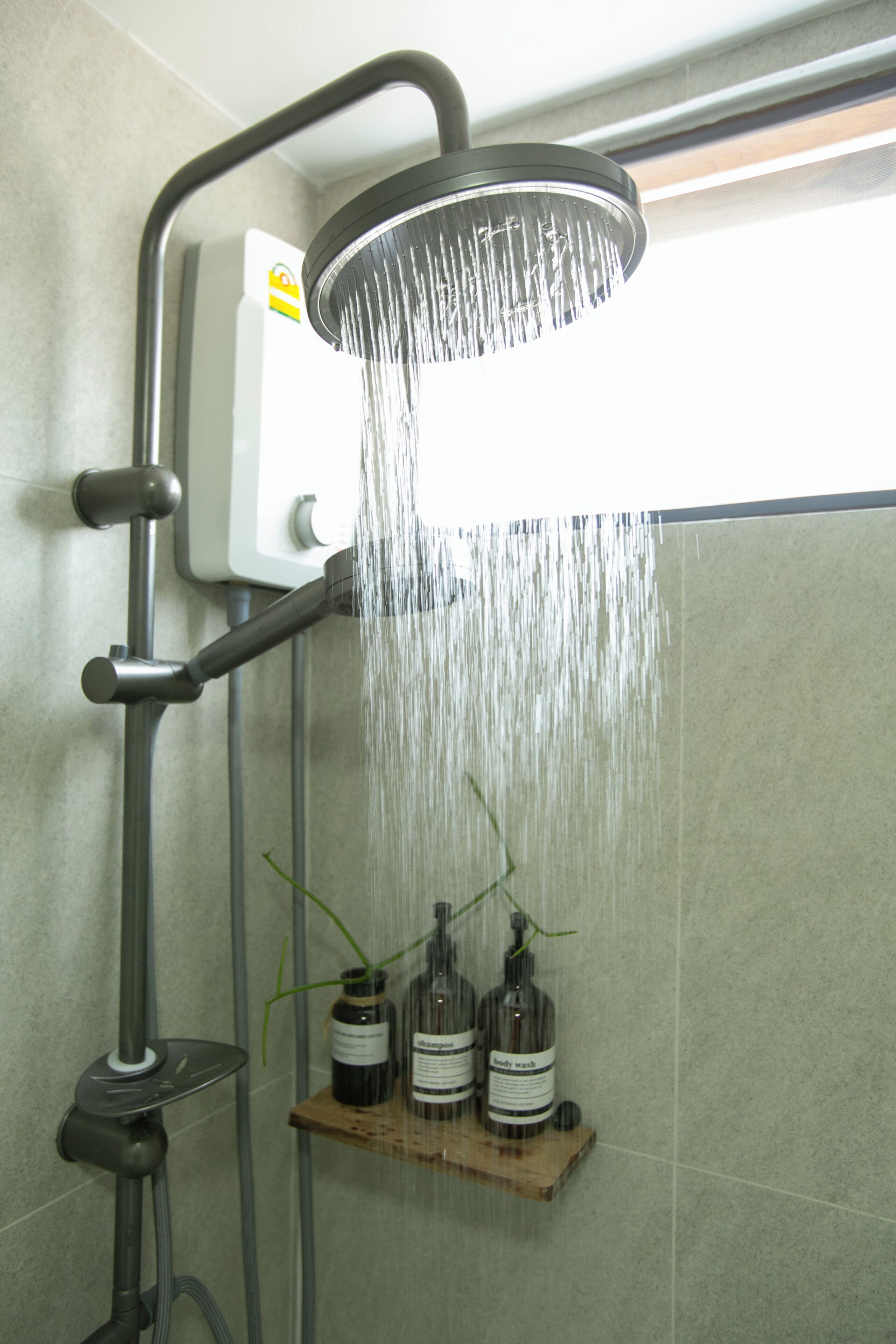 A shower with a handheld attachment, a control panel, and a shelf with bottles.