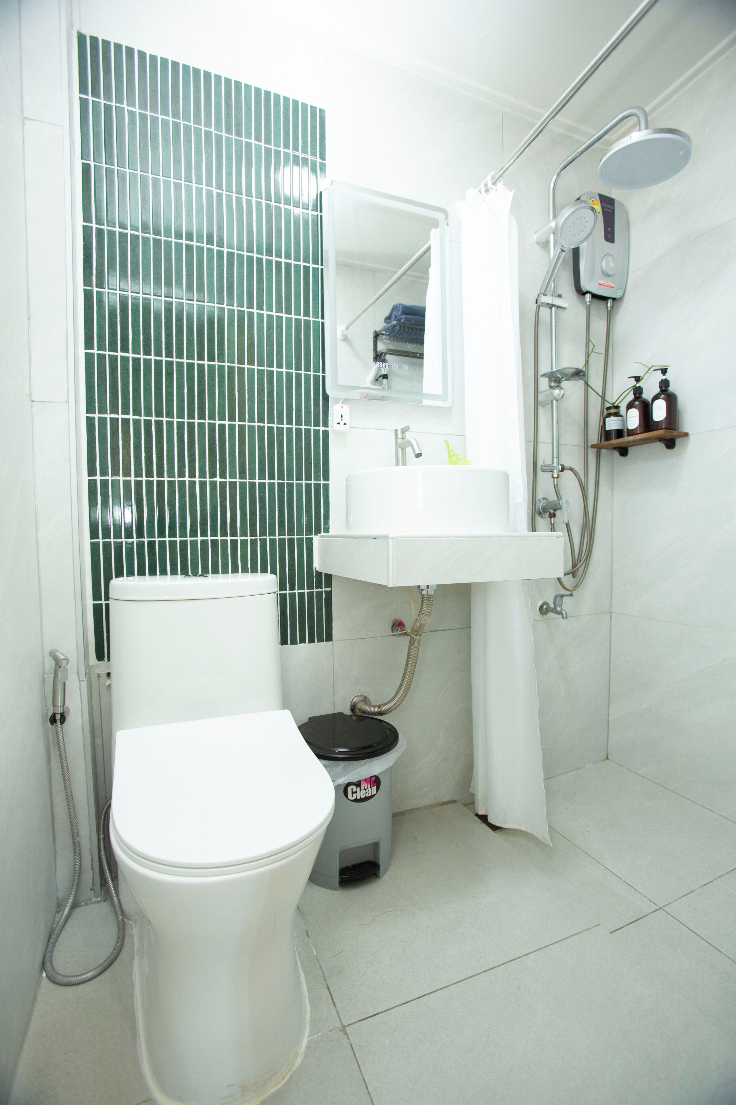 A bathroom with a toilet, sink, shower, and a mirror.