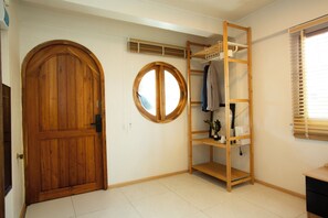 Una habitación con puerta de madera, una ventana circular, una estantería de madera y una ventana con persianas.