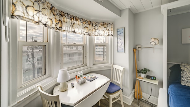 A room with a white desk, a chair, a lamp, and a window with a view of buildings. - Prime Walkable Location! 2-Unit Ocean City Getaway (Ocean City)