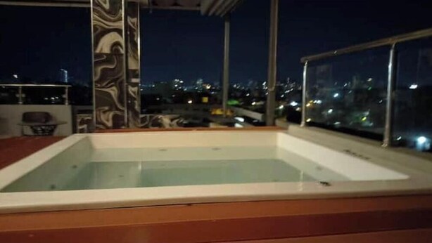 A rooftop pool with a wooden deck, surrounded by glass railings and a cityscape view. - Apt Aconchegante+Private Jacuzzi+Wi-Fi+AC in Santo Domingo RD (Santo Domingo)