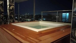 A wooden deck with a rectangular pool area, glass railings, and a cityscape view at night. - Apt Aconchegante+Private Jacuzzi+Wi-Fi+AC in Santo Domingo RD (Santo Domingo)