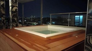 A wooden deck with a rectangular pool area, glass railings, and a cityscape view at night. - Apt Aconchegante+Private Jacuzzi+Wi-Fi+AC in Santo Domingo RD (Santo Domingo)