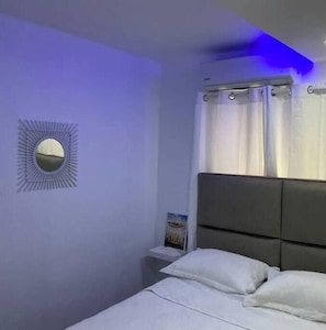 A bedroom with a bed, white pillows, a nightstand, a wall-mounted mirror, and a window with curtains. - Apartment with roof + jacuzzi + Wi-Fi + AC in Santo Domingo RD (Santo Domingo)