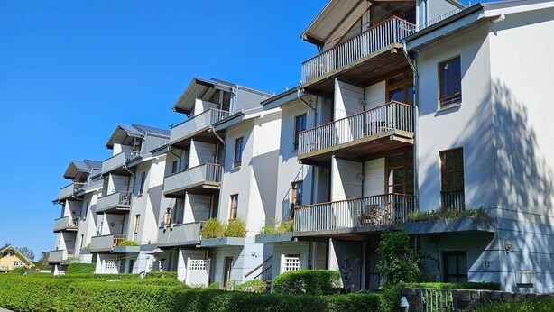 Une rangée d’immeubles modernes à plusieurs étages, dotés de balcons, sous un ciel bleu dégagé, et entourés d’un espace vert bien entretenu.
