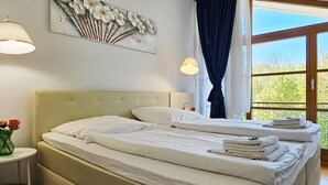 Une chambre d’hôtel avec deux lits, un tableau au mur, une fenêtre avec des rideaux et un vase de fleurs sur une table d’appoint.