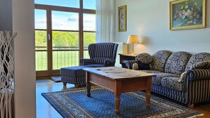Une pièce avec une grande fenêtre, un canapé, un fauteuil, une table et une lampe.