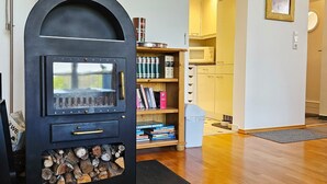 Une cuisine moderne équipée d’un poêle à bois encastré, d’étagères en bois où sont rangés des livres et d’un four à micro-ondes.