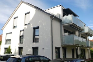 Een modern gebouw met twee verdiepingen, een plat dak, grote ramen en een balkon op de bovenste etage.