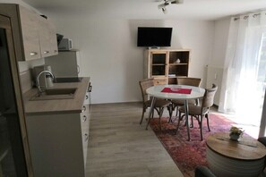 Een ruimtelijk ingerichte leefruimte met kitchenette, eethoek en een aan de muur bevestigde televisie.